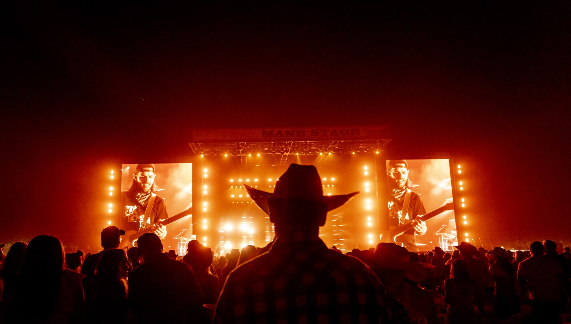 A person in a cowboy hat looks toward the brightly lit stage