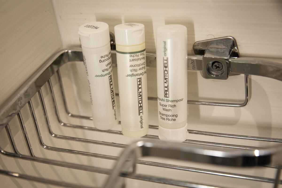 Small plastic bottles of shampoo and conditioner sit inside a shower in a Marriott hotel room.