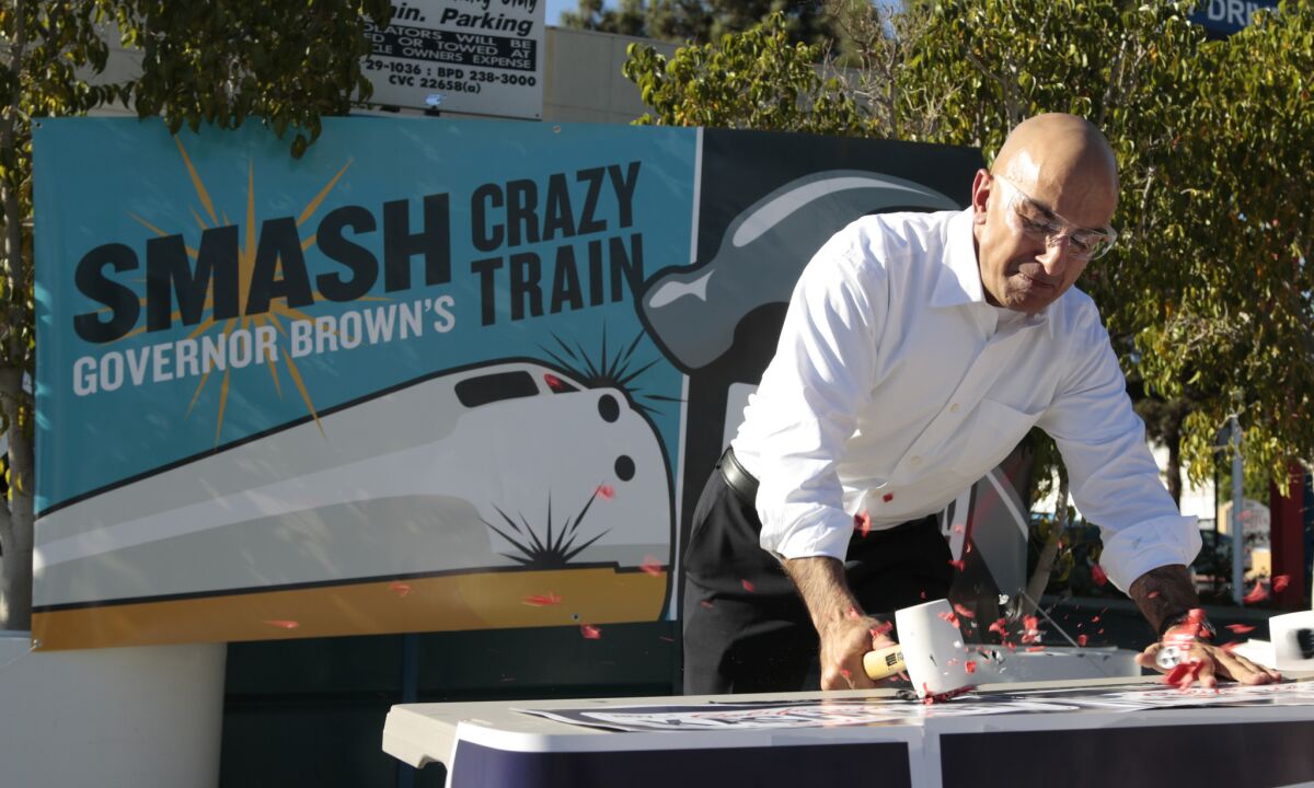 Republican gubernatorial candidate Neel Kashkari smashes a plastic toy train at a Mobil gas station in Burbank, saying he was sending a message to Gov. Jerry Brown to "stop the crazy train."