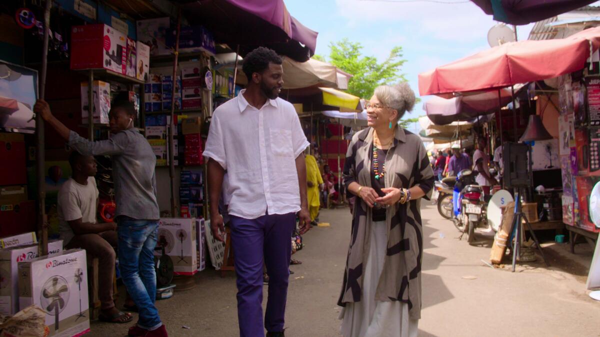 Stephen Satterfield and Dr. Jessica B. Harris walk between rows of market stalls.