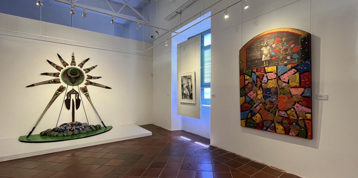 An assemblage made out of fragments of coconut trees and a colorful painting are presented in a museum gallery