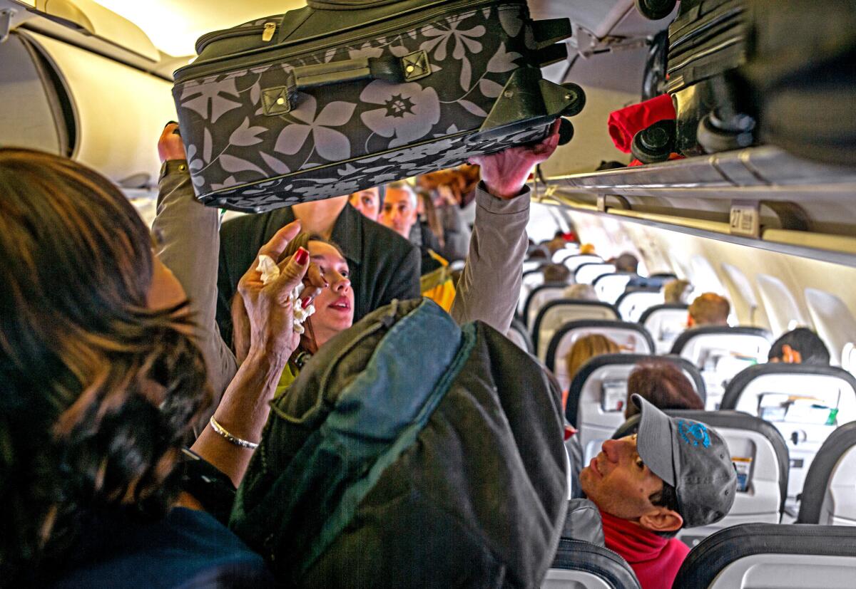 Passengers load carry-on bags into overhead bins on a United Airlines flight. Check-bag fees reduce the amount of checked luggage, cutting delays and lost-bag complaints, studies find.