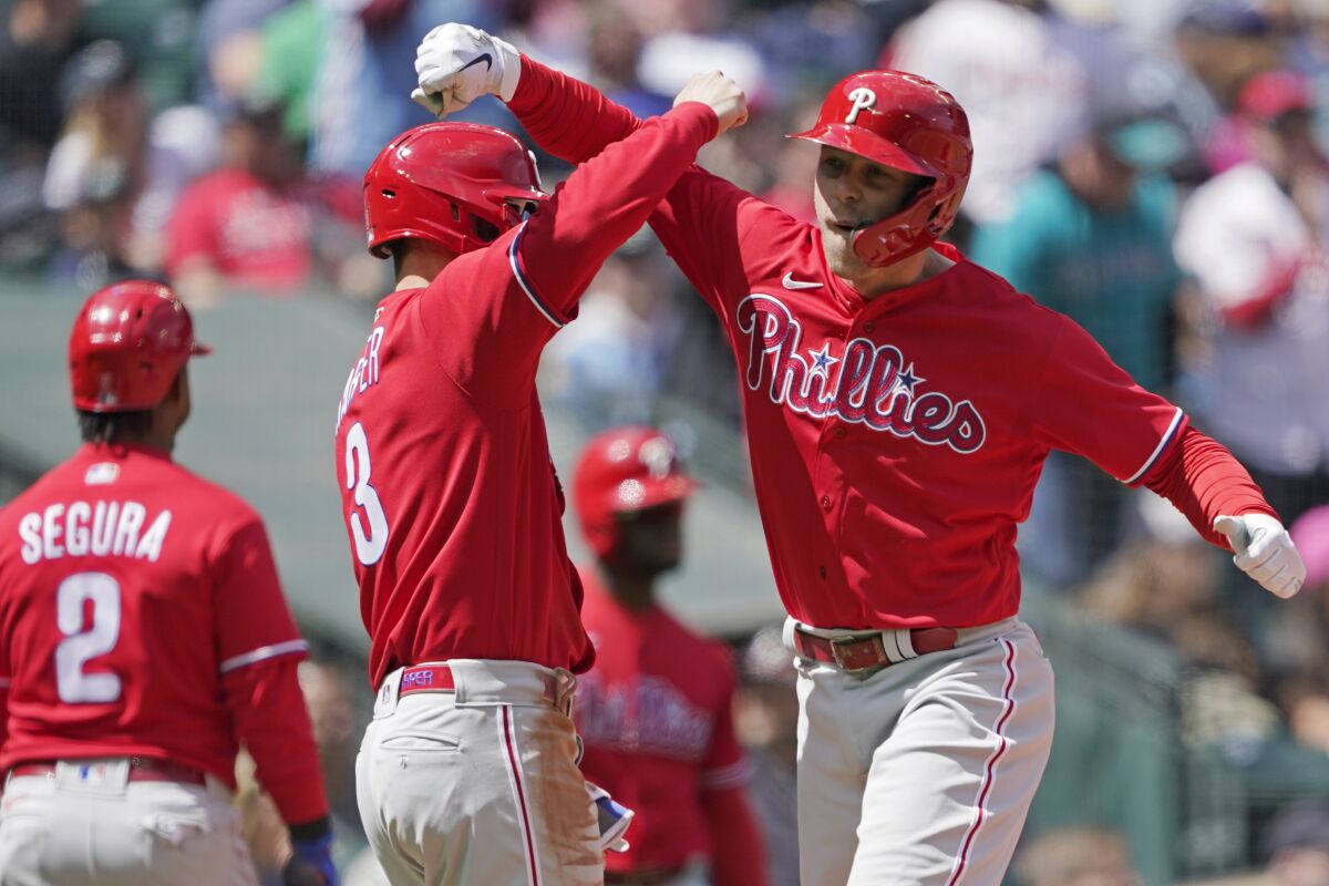 Philadelphia Phillies' Rhys Hoskins, right, is greeted by Bryce Harper, center, at the plate after Hoskins hit a grand slam against the Seattle Mariners to score Harper during the fourth inning of a baseball game, Wednesday, May 11, 2022, in Seattle. (AP Photo/Ted S. Warren)
