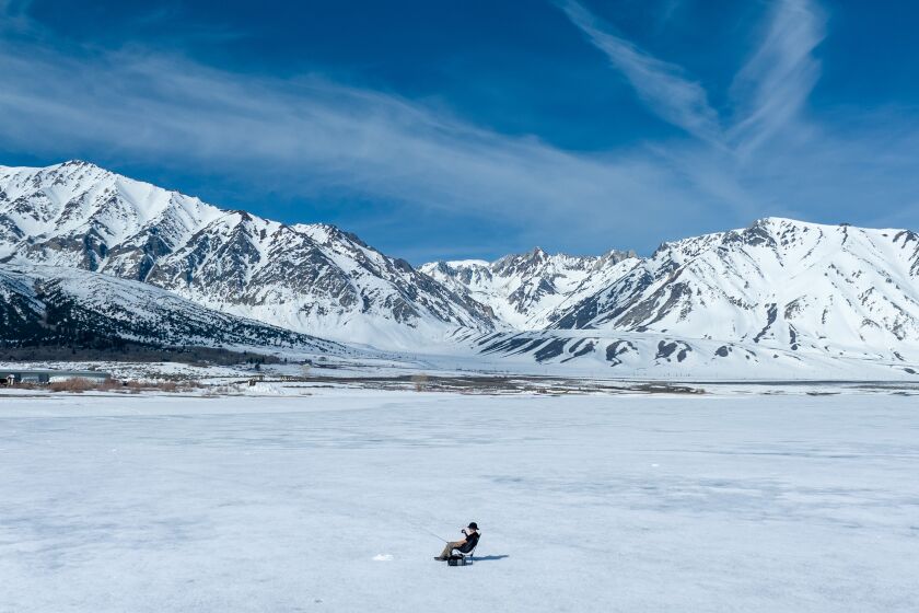 CROWLEY LAKE, CA - April 29: An ice fisherman waits for a bite as his line is dropped into a hole in a frozen Crowley Lake on the official opening day of Eastern Sierra trout season Saturday, April 29, 2023 in Crowley Lake, CA. Ice fishing was the only option on the lake as the marina was still frozen. (Brian van der Brug / Los Angeles Times)