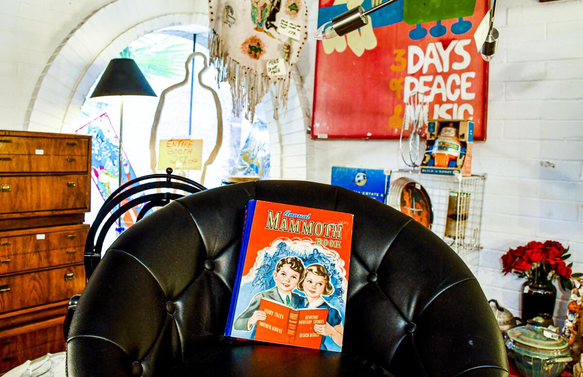 A book is propped up on a chair in front of a chest of drawers, a lamp, wall art and more