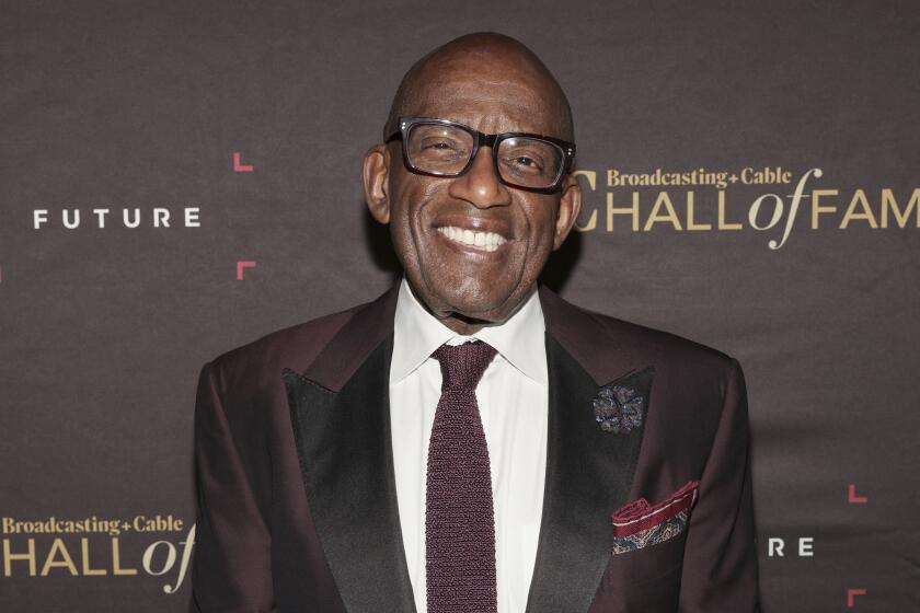 Al Roker in eyeglasses and a dark suit smiles broadly against a promotional backdrop