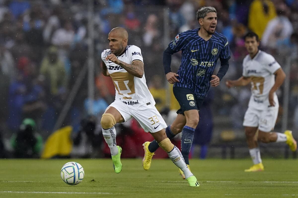 El brasileño Dani Alves, de los Pumas, conduce el balón junto a Diego Valdés, del América,