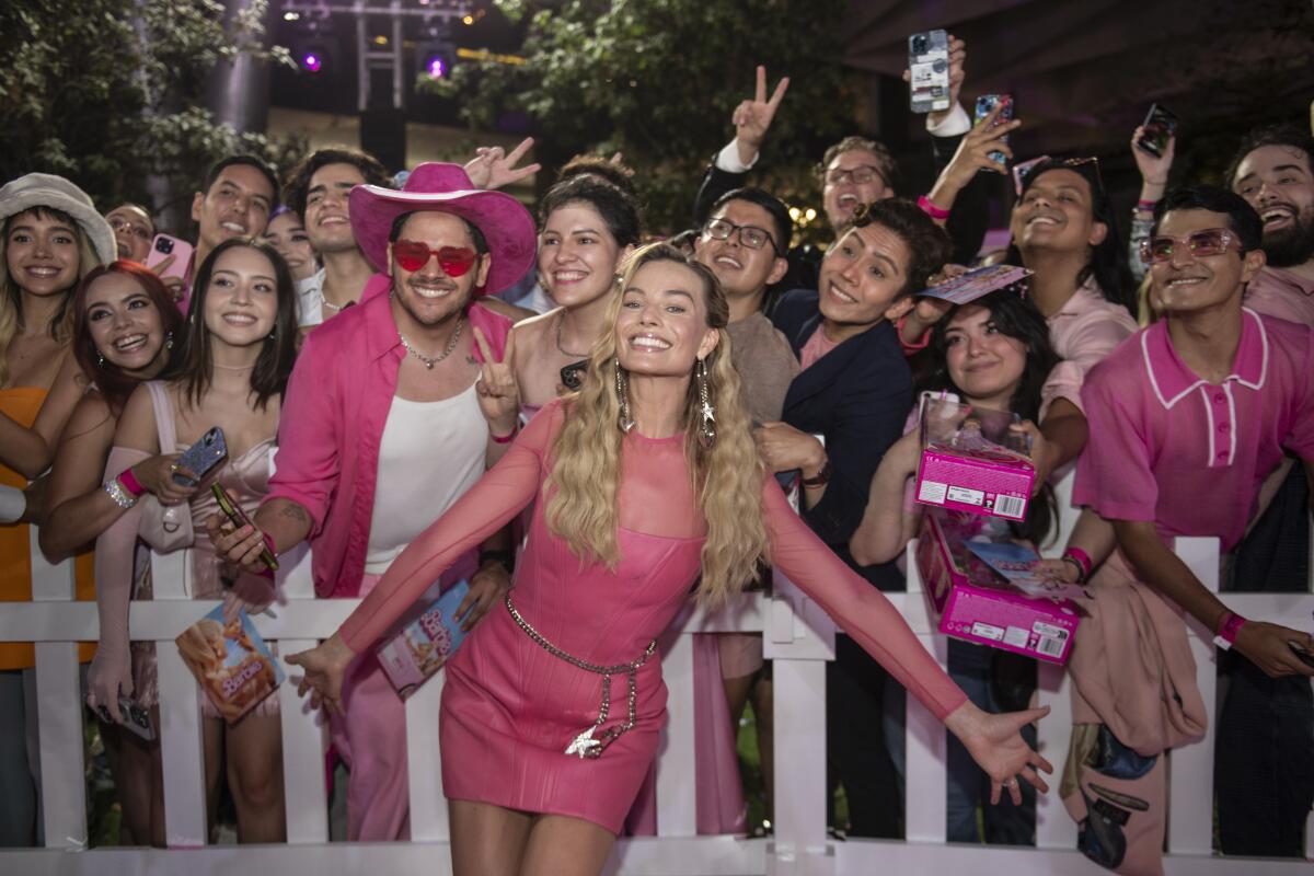Margot Robbie in a pink leather minidress with a crowd of fans behind her.