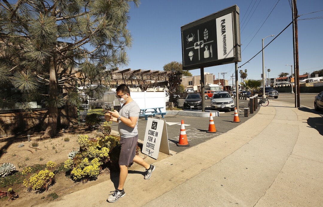 These parts of L.A. barely felt the winter coronavirus
surge. Here is why they were spared 3 A man in a mask looks at his phone while walking on the sidewalk with a coffee in hand