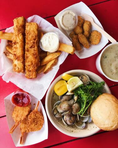 A tray of fish and chips, clams, chowder and fried oysters on a red wood picnic table at Malibu Seafood.