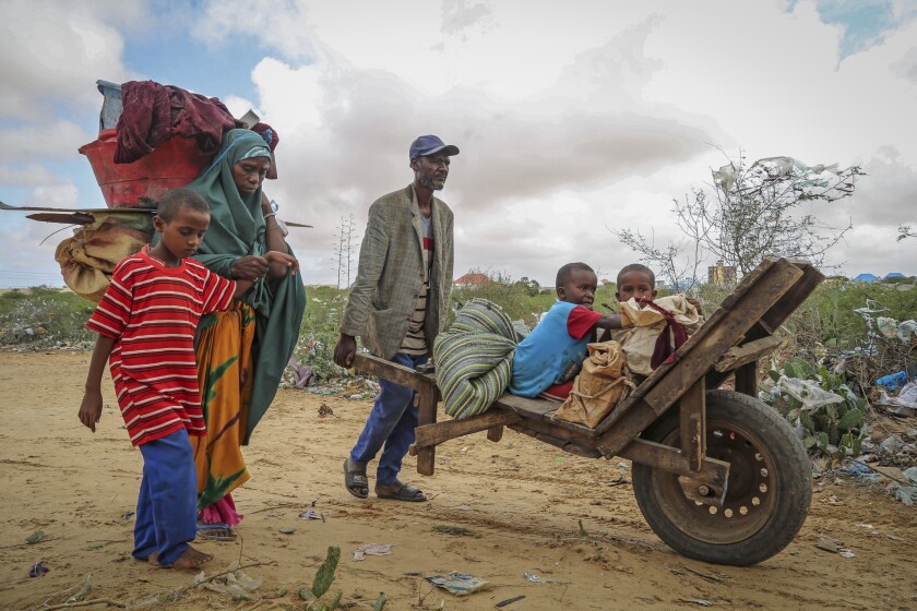 A local resident uses a wheelbarrow to transport the young children of a woman who fled drought-stricken areas as she arrives at a makeshift camp for the displaced on the outskirts of Mogadishu, Somalia Thursday, June 30, 2022. The war in Ukraine has abruptly drawn millions of dollars away from longer-running humanitarian crises and Somalia is perhaps the most vulnerable as thousands die of hunger amid the driest drought in decades. (AP Photo/Farah Abdi Warsameh)