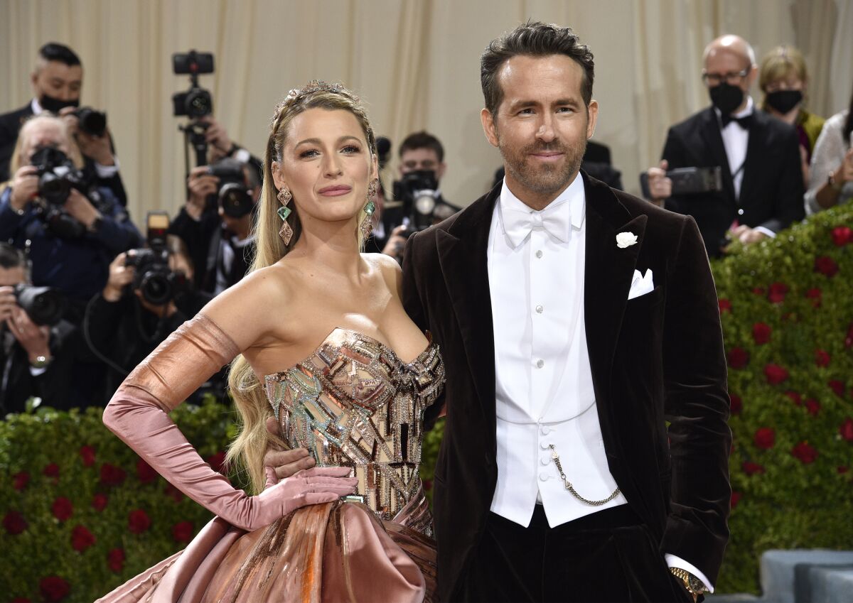 A woman in a formal gown and a man in a tux with white bow tie pose with photographers behind them