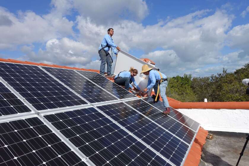 Workers install solar panels on a rooftop on Feb. 20 at a home in Palmetto Bay, Florida.