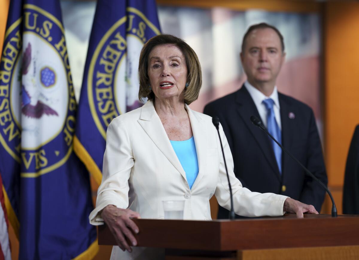 A woman at a podium with flags behind her and a man standing beside her.