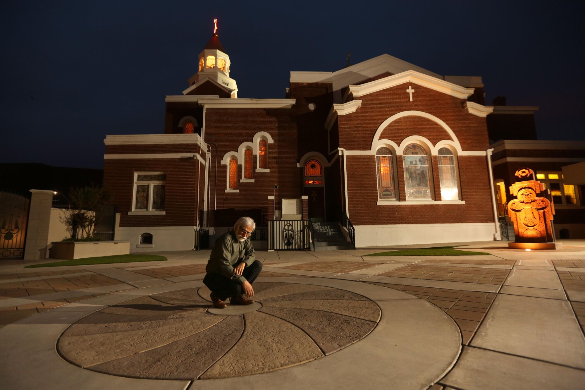 Varoujan Der Simonian kneels in the center of a concrete design outside a church