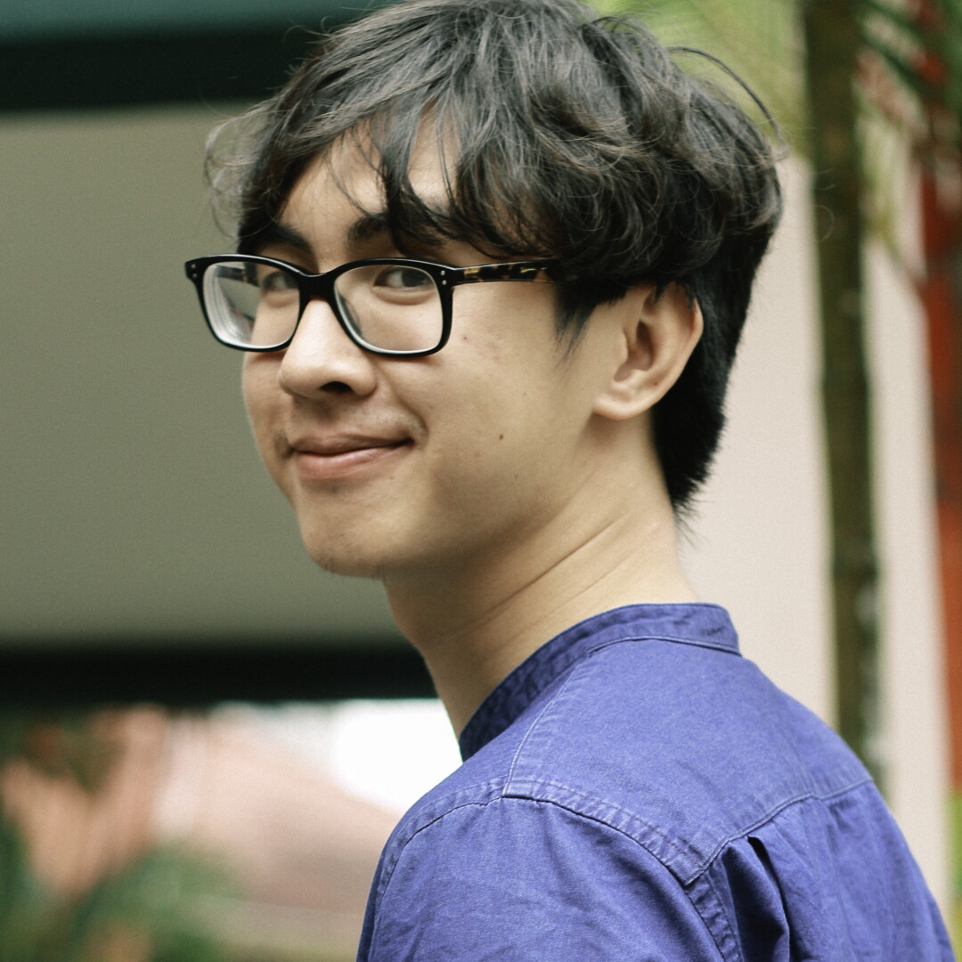 A smiling young man with glasses and tousled dark hair.