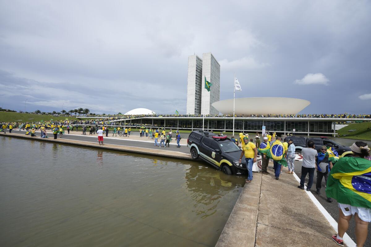 A police car is shown its nose tipped into a public fountain before Brasilia's space-age congressional buildings