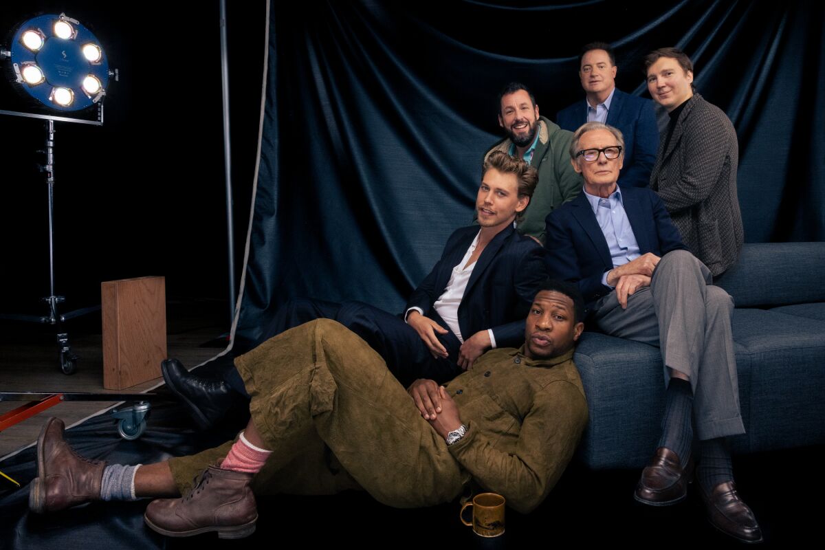A group of six actors, five seated around the sixth.