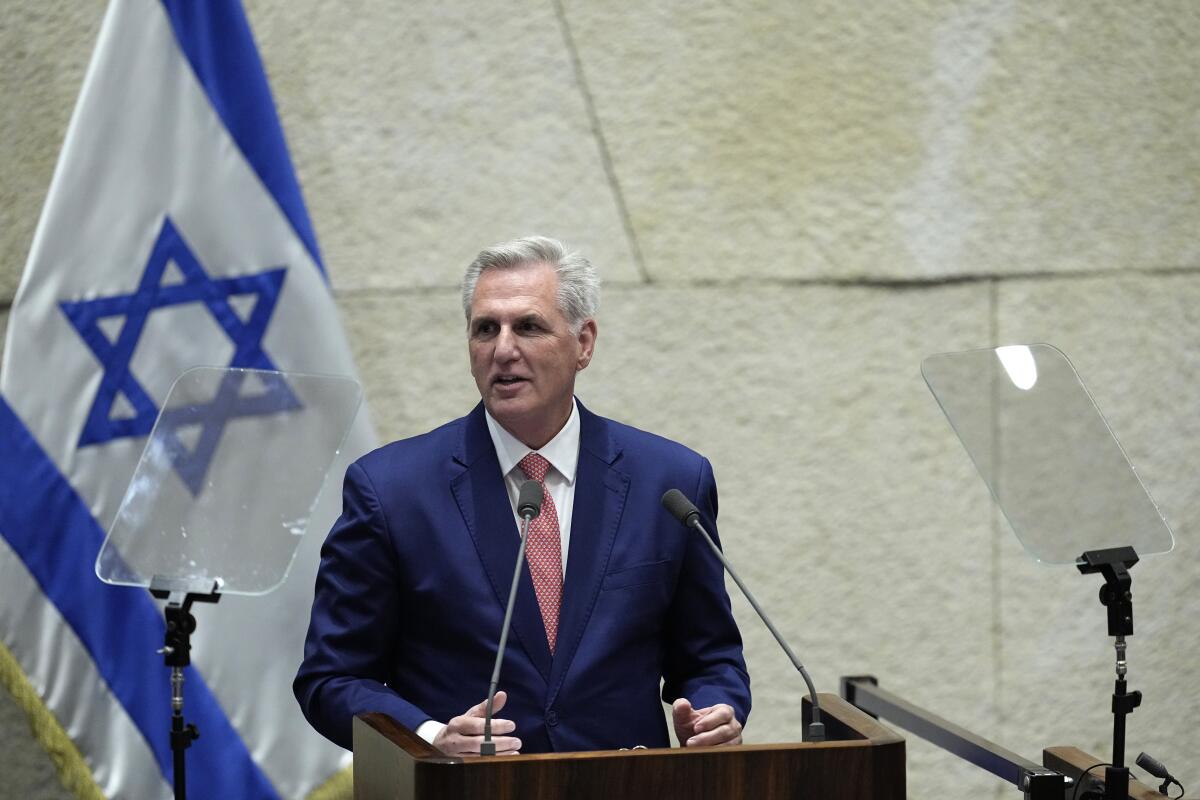 House Speaker Kevin McCarthy at a microphone next to an Israeli flag.