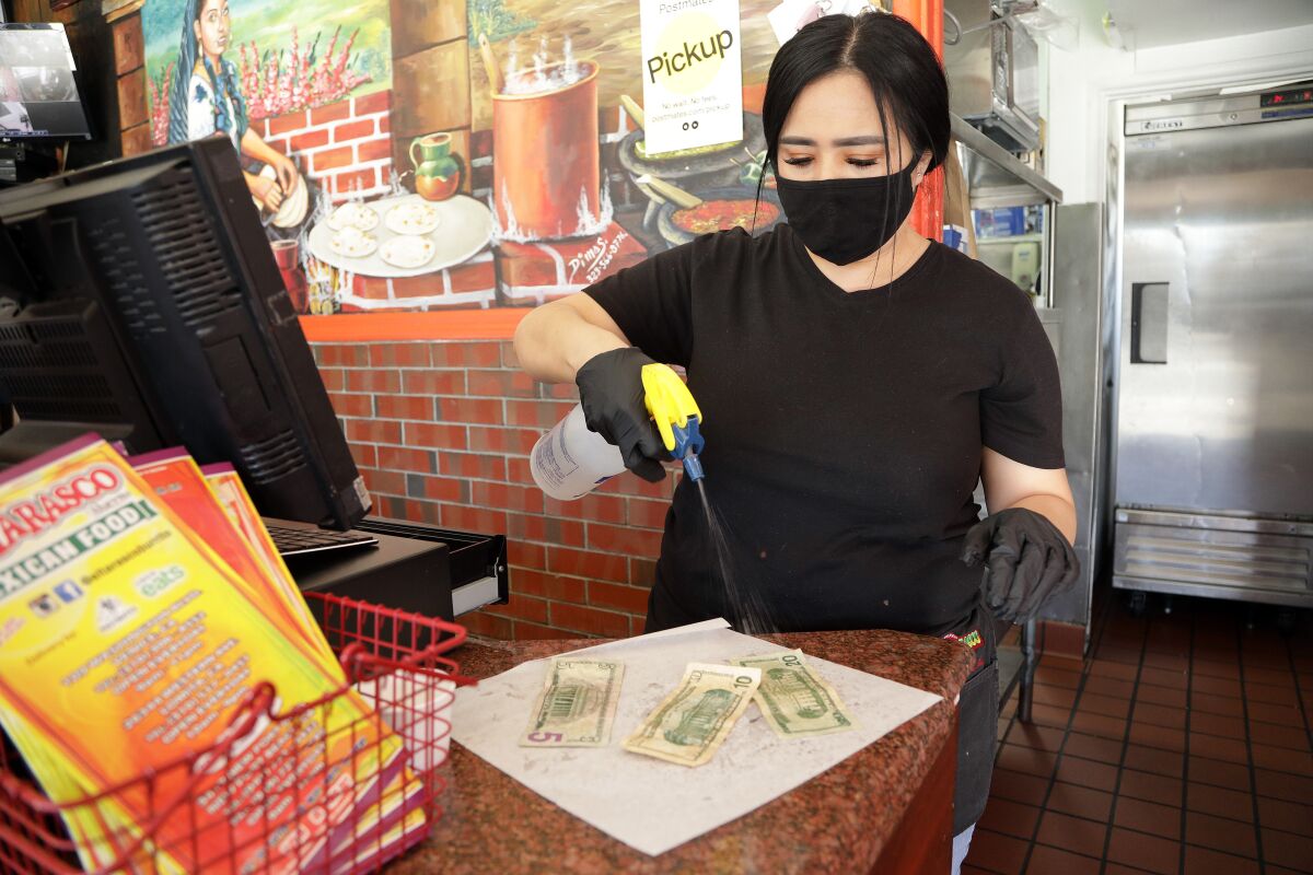 Maricela Moreno, a cashier at El Tarasco in Marina del Rey, sprays bills with alcohol at the restaurant. She said a lot of customers pay with Apple Pay or credit cards.