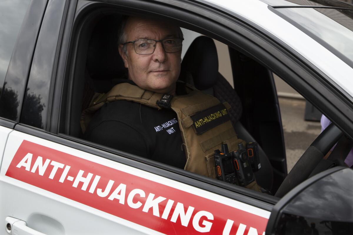 A man sits in a car in a vest. The car has Anti-Hijacking Unit written on it. 