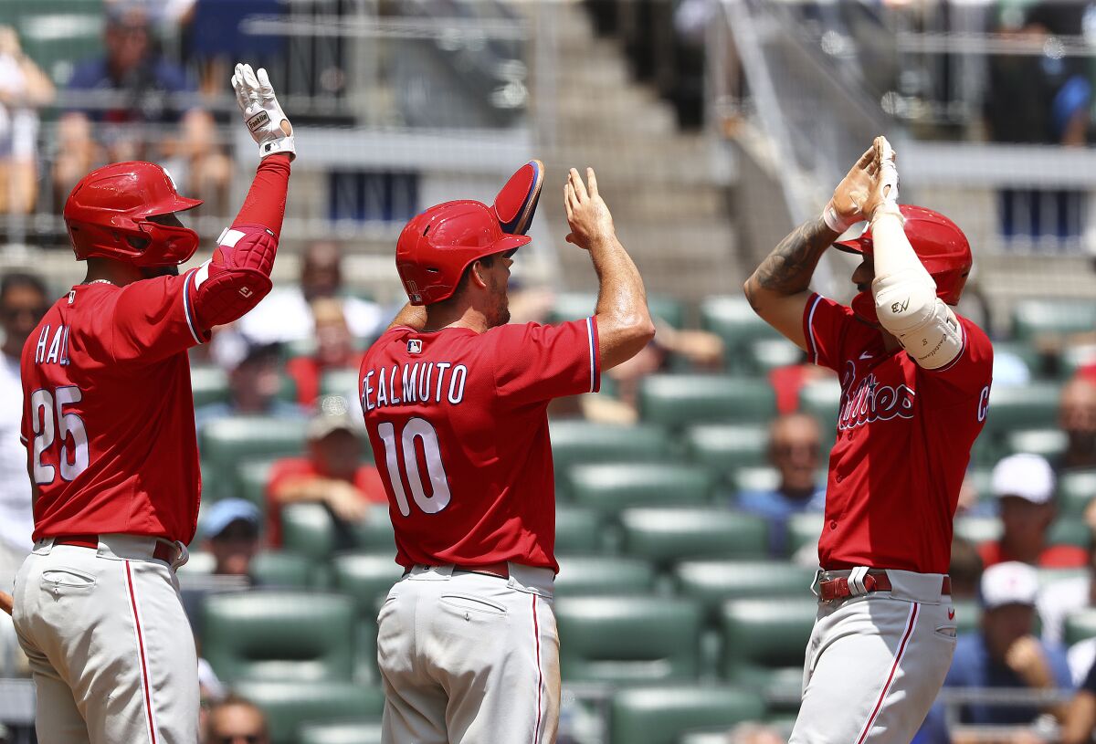 Philadelphia Phillies players, from left, Darick Hall and J.T. Realmuto greet Nick Castellanos on his three-run home run in the eighth inning of a baseball game against the Atlanta Braves, Wednesday, Aug. 3, 2022, in Atlanta. (Curtis Compton/Atlanta Journal-Constitution via AP)