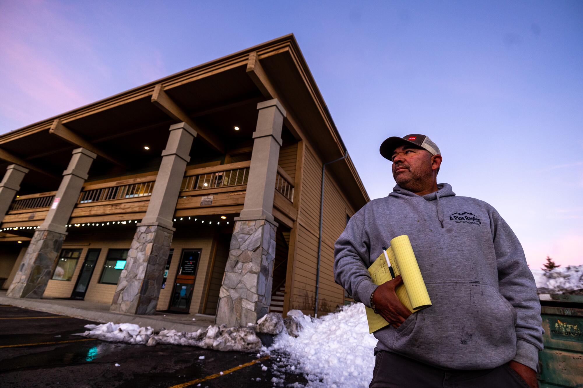 A contractor stands holding a yellow legal pad outside a building.