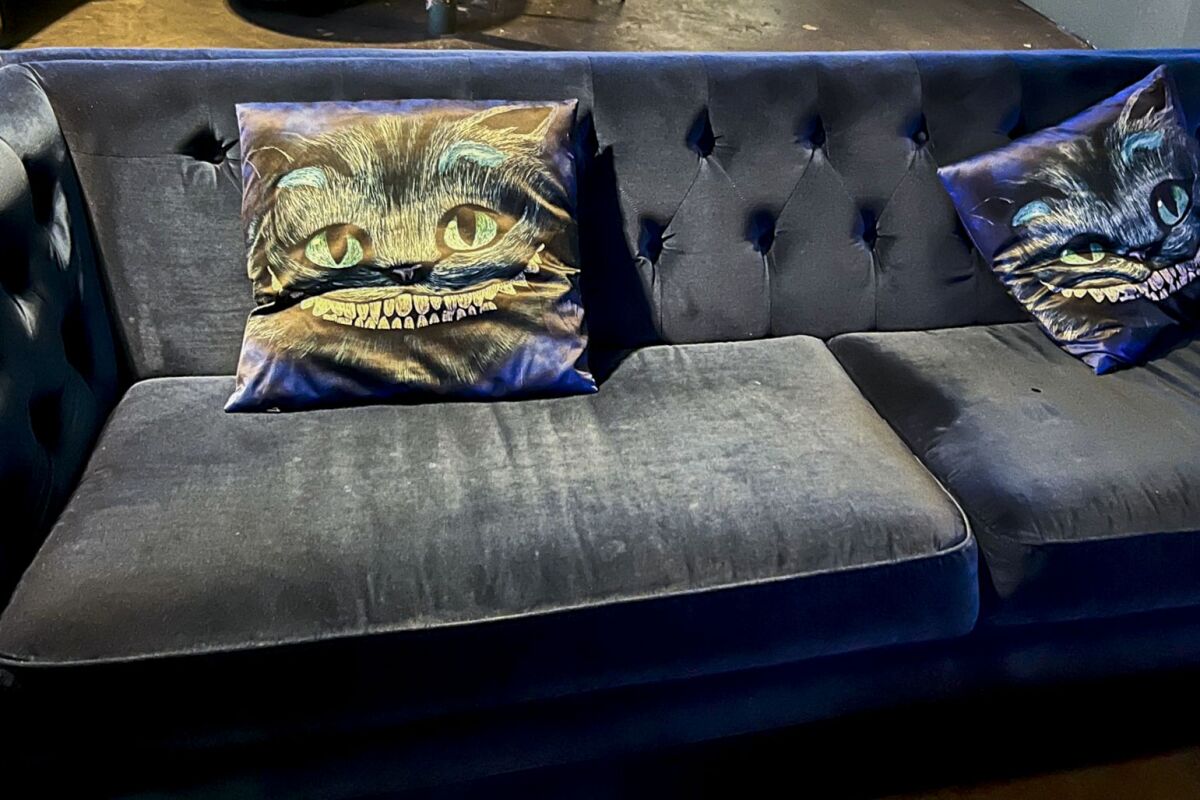 A velvet couch with grinning Cheshire cat pillows.