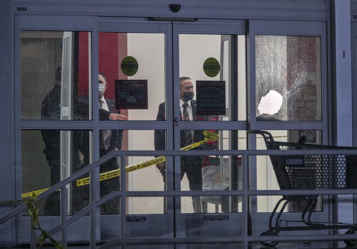 Three people stand behind glass doors at an entrance. One pane has a hole.