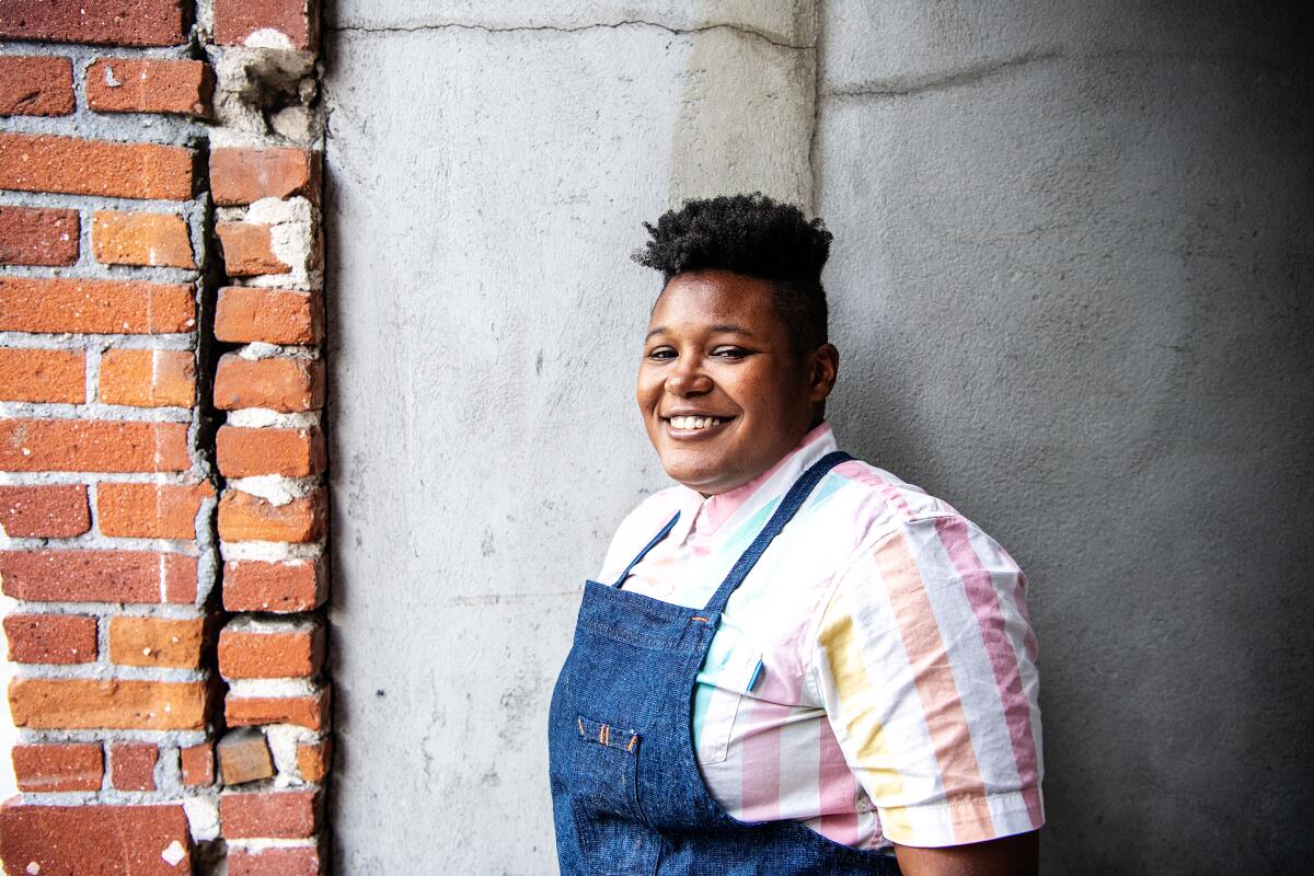 Rashida Holmes, chef and owner of Bridgetown Roti, stands in an apron against a brick wall