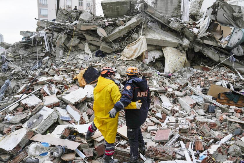 Emergency team members before massive piles of rubble while searching for people in a destroyed building in Adana, Turkey