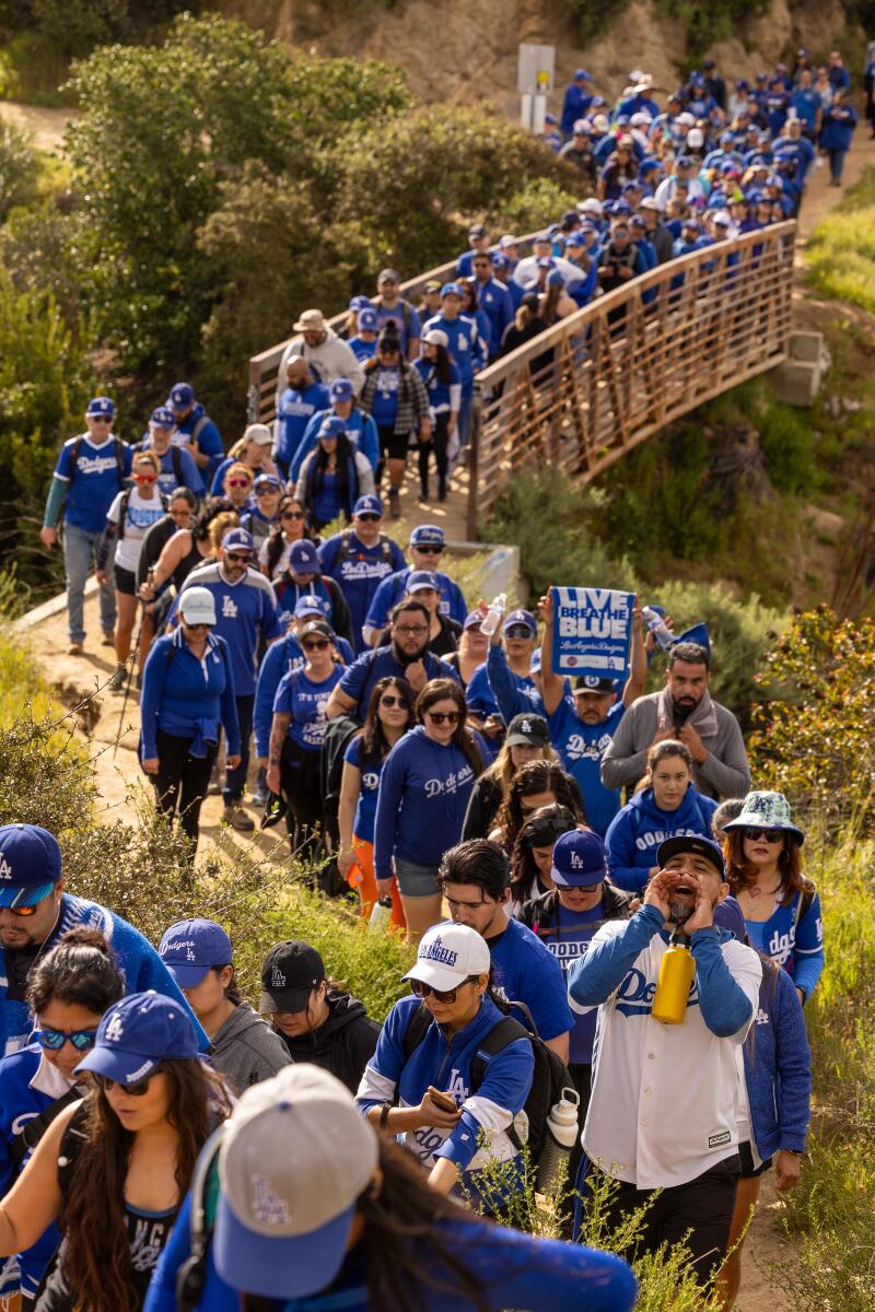 Crowds of hikers, including the Dodger blue hiking team, cross a bridge.