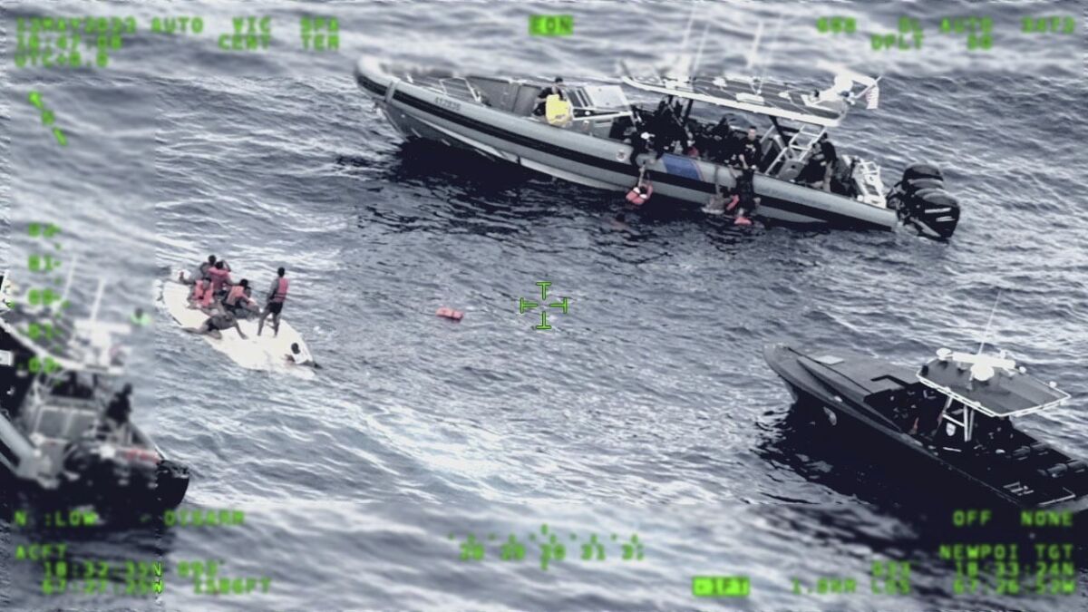 This photo released by the Seventh U.S. Coast Guard District shows people standing on a capsized boat, left, as some of its passengers are pulled up on to a rescue boat, top, in the open waters northwest of Puerto Rico, Thursday, May 12, 2022. Some people have been rescued while others were found dead after the boat carrying suspected migrants capsized. The boat was first spotted by U.S. Customs and Border Protection. (Seventh U.S. Coast Guard District via AP)