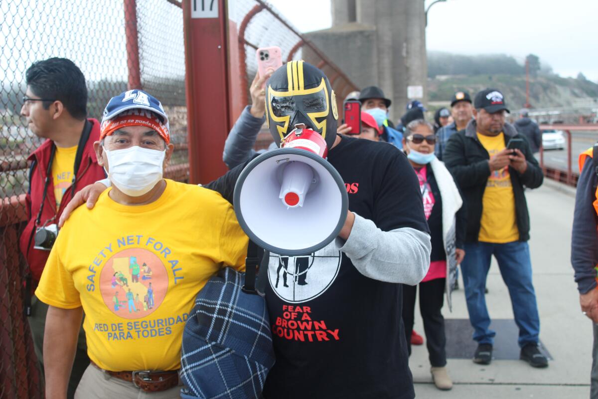 A man in a mask speaks into a megaphone at a rally.