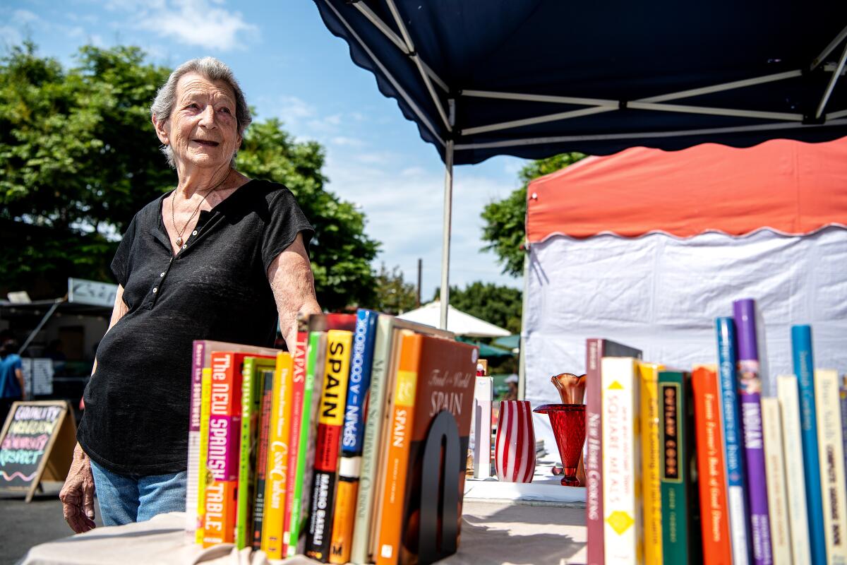 A woman stands next to a table filled with cookbooks. 