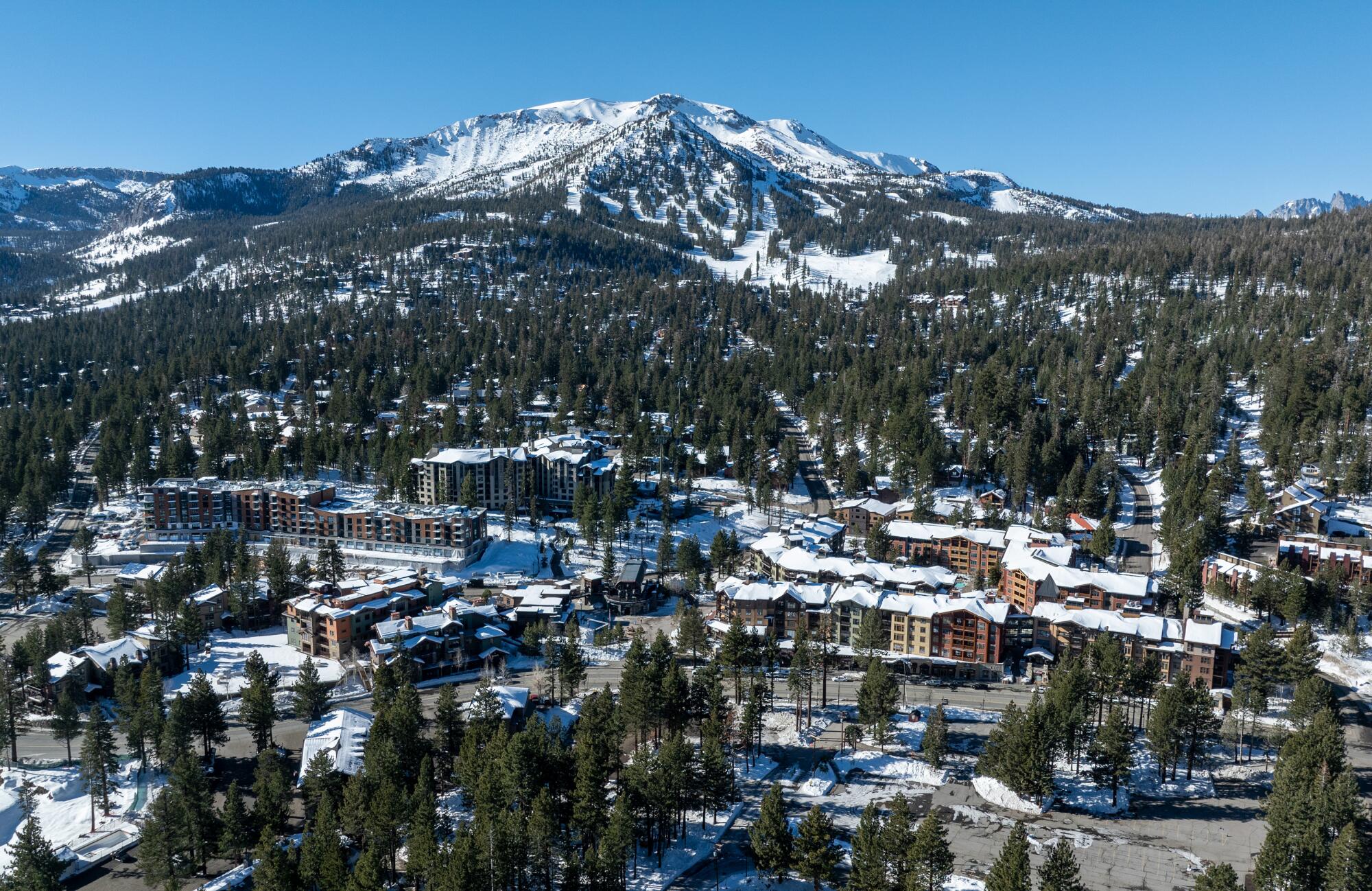 An aerial photo of snow-topped hotels, shops and restaurants with Mammoth Mountain in the background.
