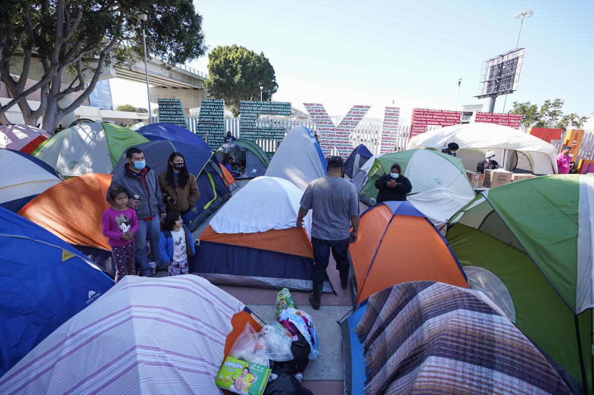People amid colorful tents in Tijuana. A sign in the background says MEXICO.