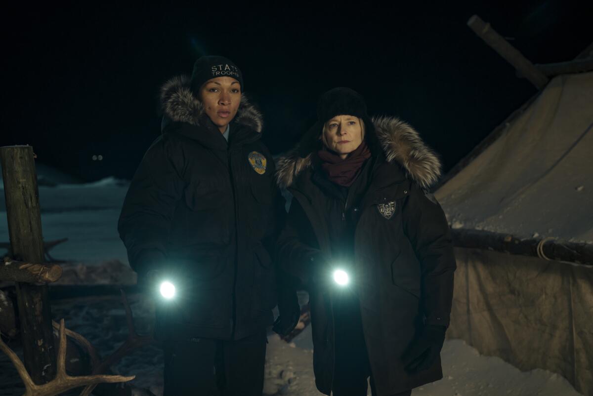 Two women in parkas shine flashlights in the snow-covered darkness.