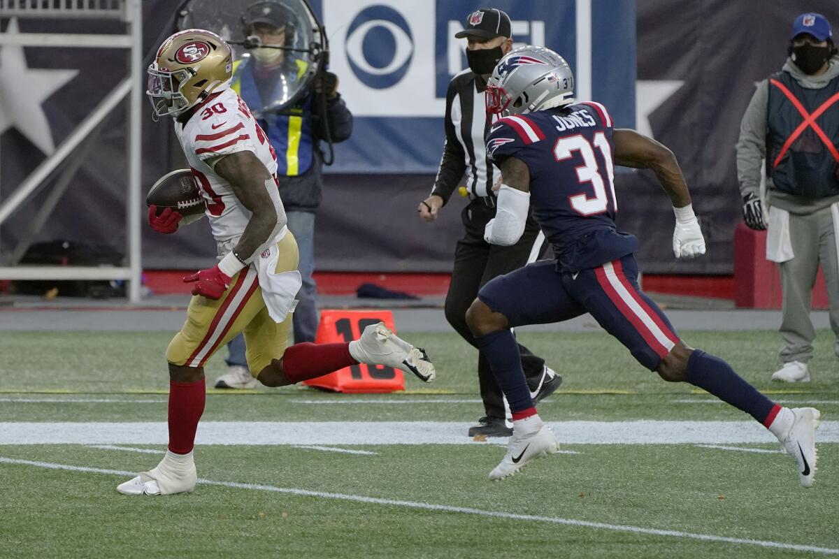 San Francisco 49ers running back Jeff Wilson Jr. runs in front of New England Patriots defensive back Jonathan Jones.