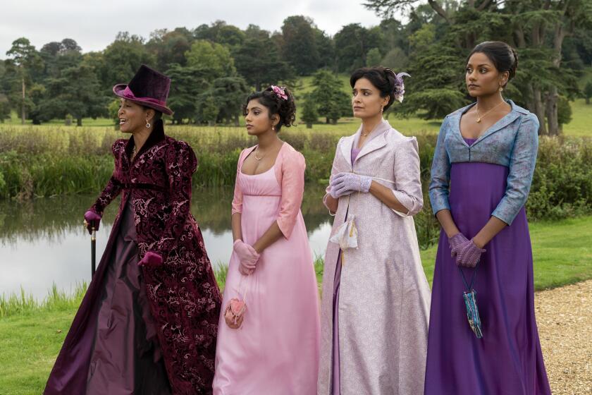 Four women in ornate dresses standing by a lake