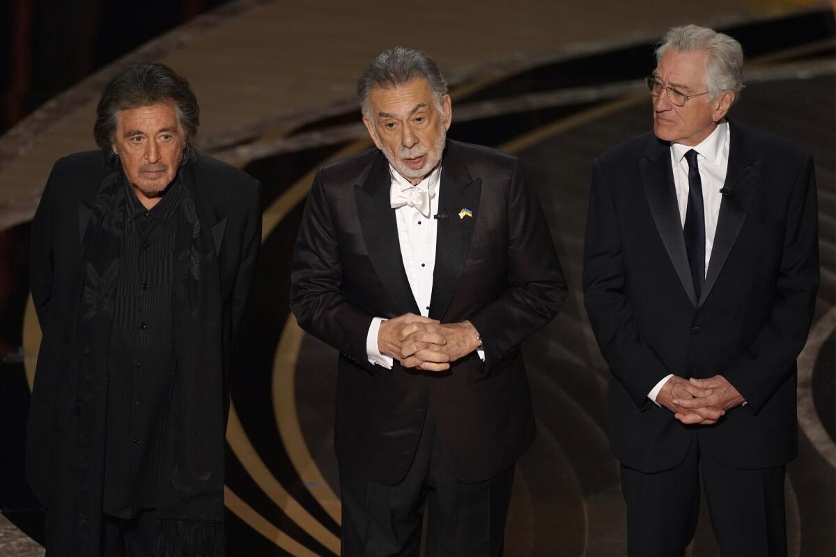 Three men in tuxedos stand onstage