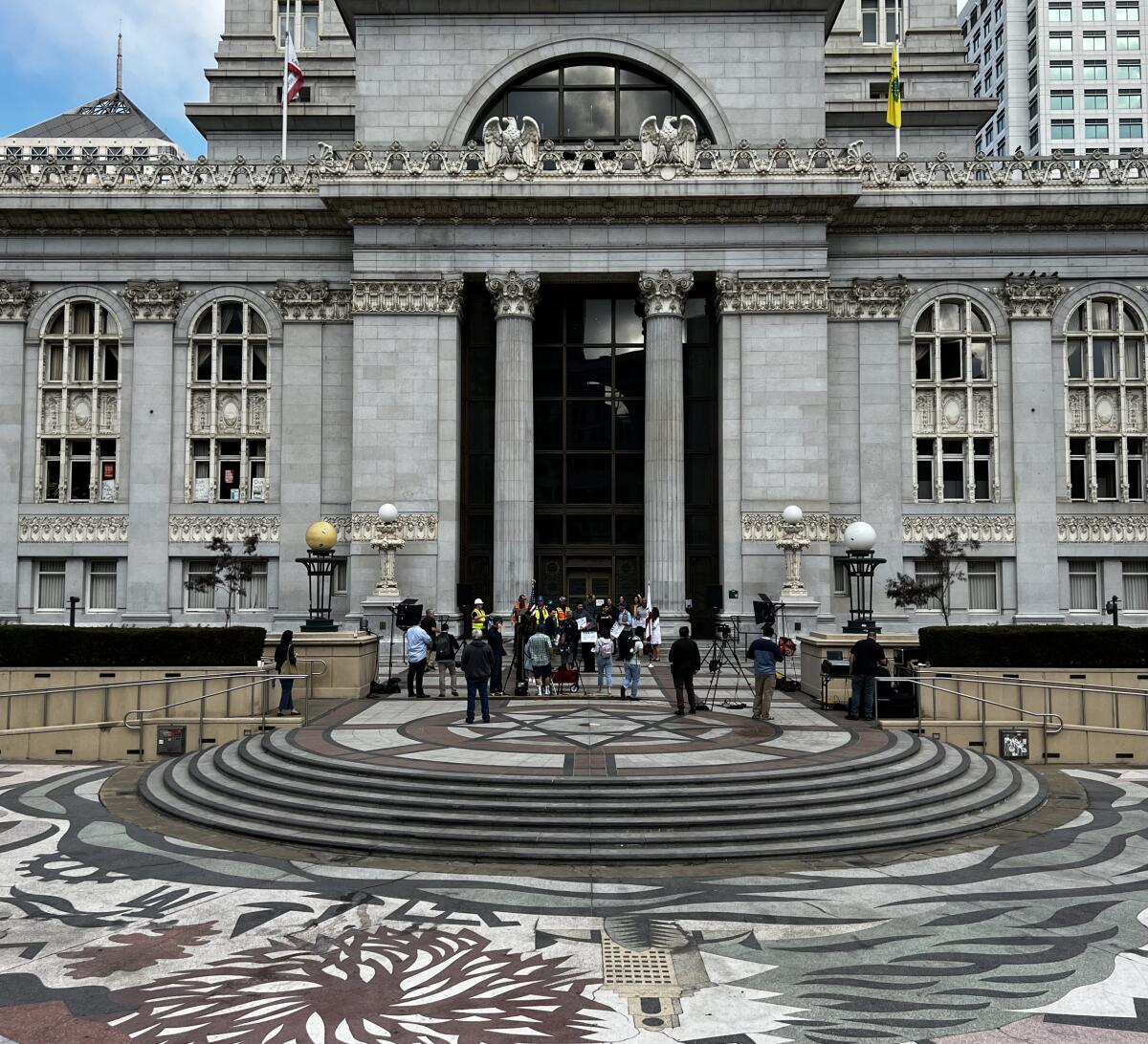 People stand in front of a grand, gray building.