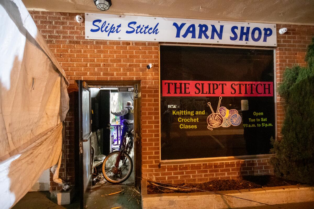 A sheriff's detective stands in the open doorway of a brick building signed as the Slipt Stitch Yarn Shop.