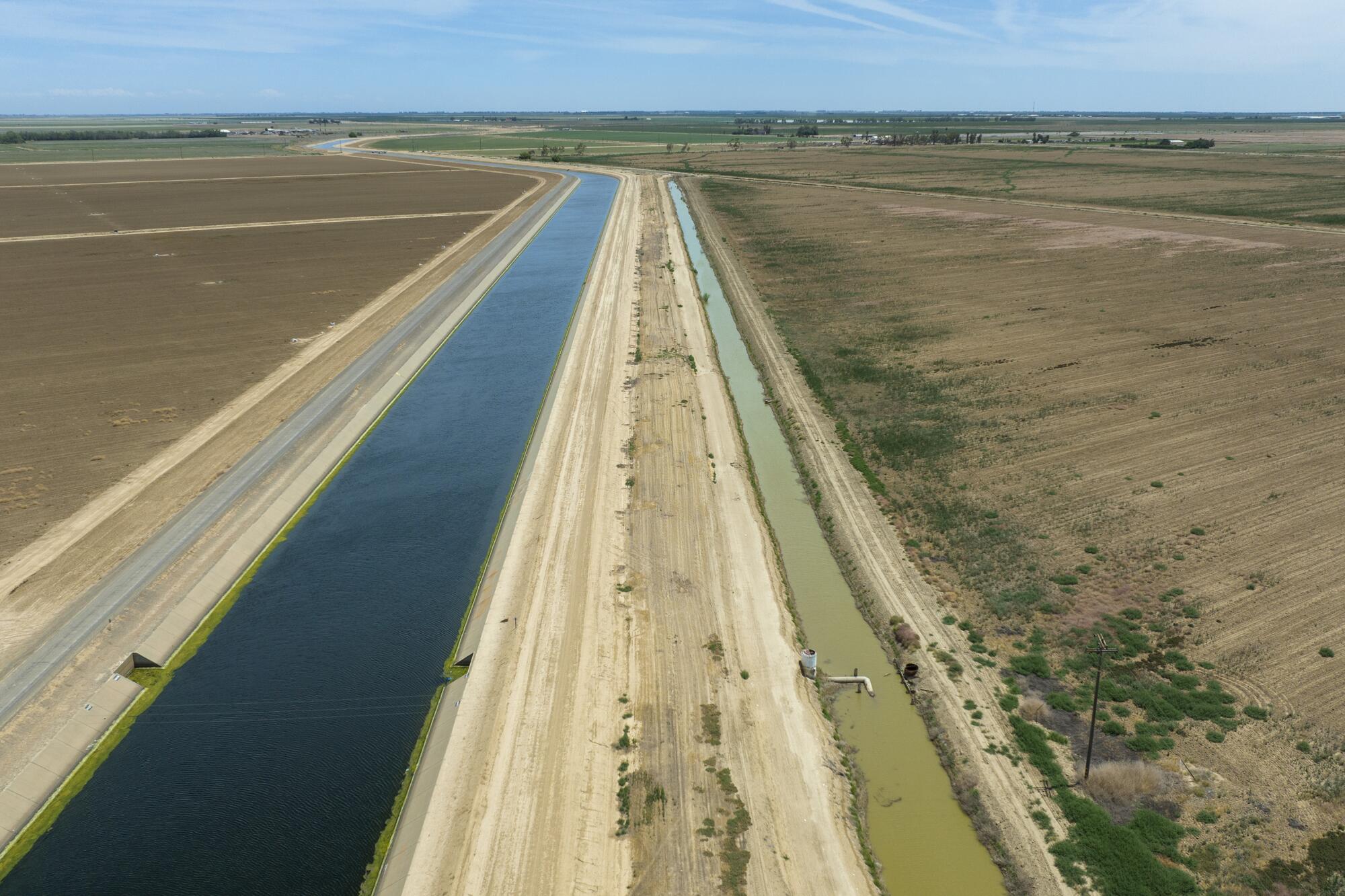 A large canal and smaller irrigation channel run parallel to one another across dusty farmland.