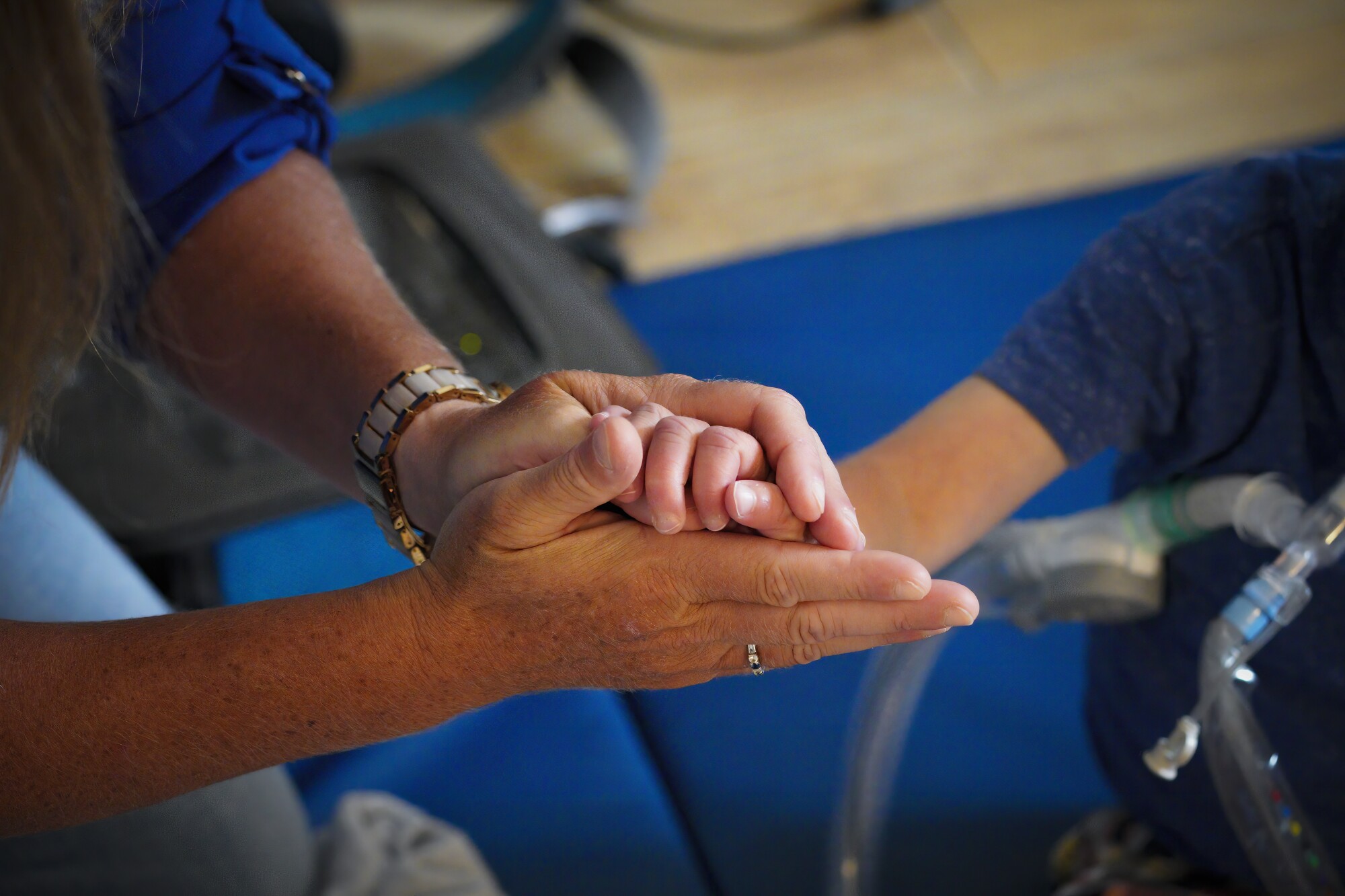 Ali Tebbs holds the hand of her son, Samuel, before attaching his feeding tube.