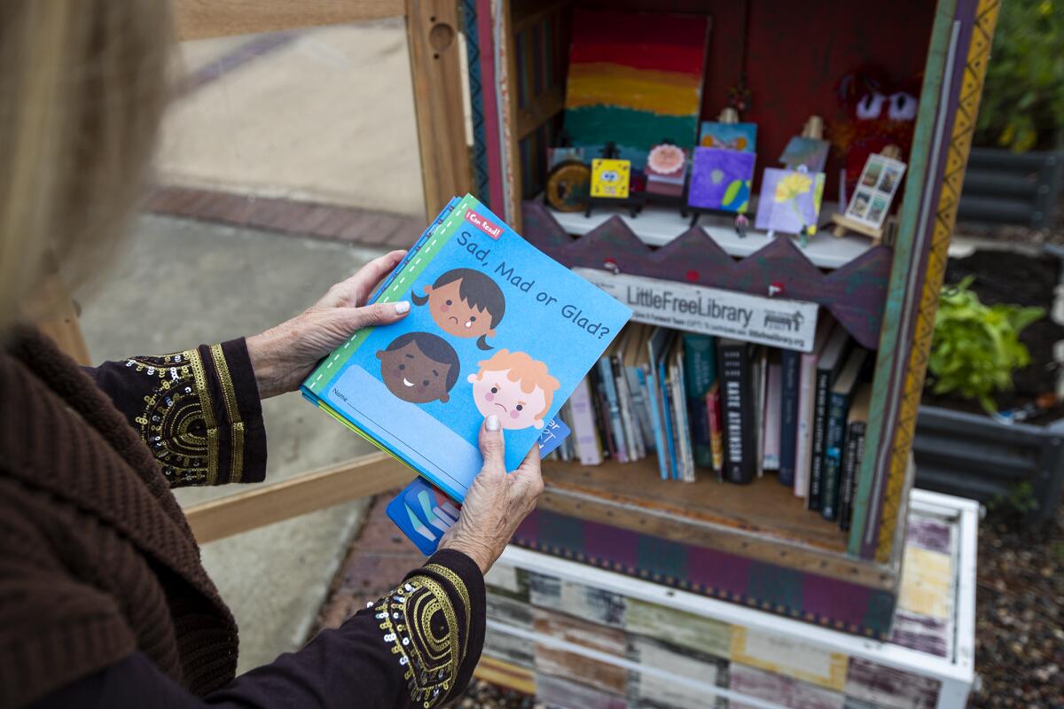 Charlene Ashendorf looks at several books left in her Little Free Library at her home in Costa Mesa.