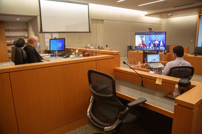 Judge Jay Bloom seated at his courtroom bench, looking at big TV screen during video conference call