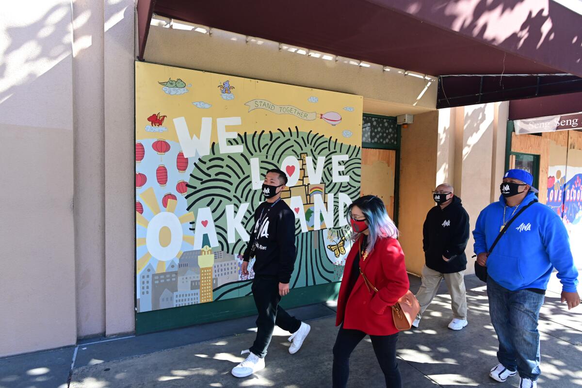 Four people walk in front of a mural that says We Love Oakland