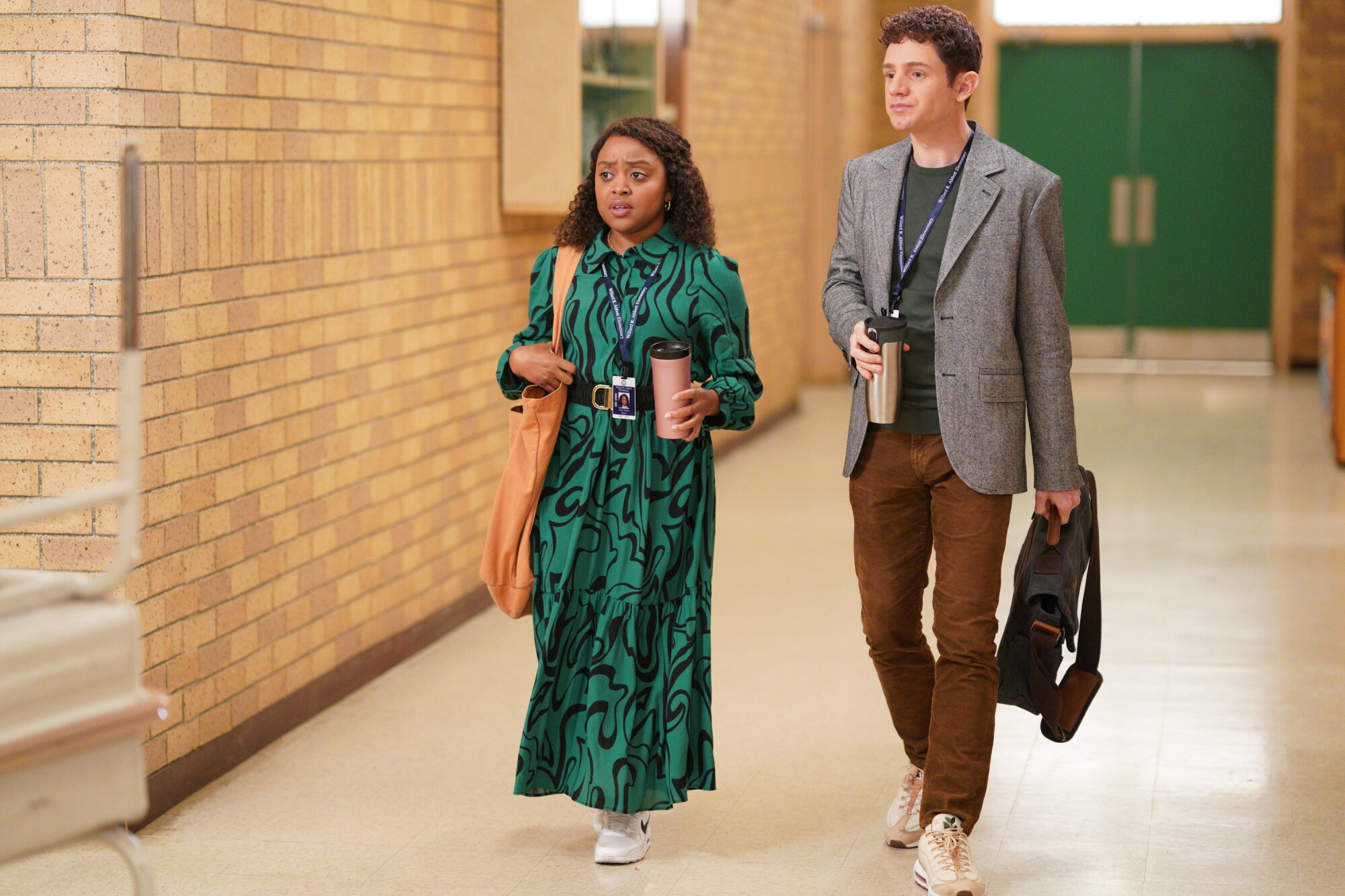Two people walk down a school hallway in a scene from 