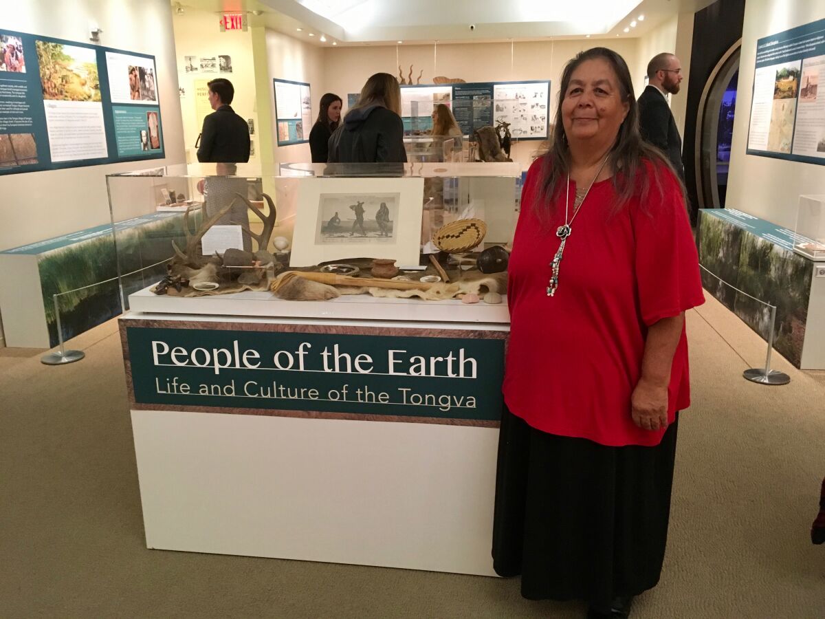 Julia Bogany stands inside a museum next to a sign that says "People of the Earth: Life and Culture of the Tongva."